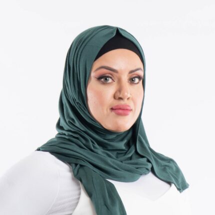 Woman wearing a deep forrest green premium jersey hijab styled with an elegant front drape, demonstrating the soft and opaque fabric.